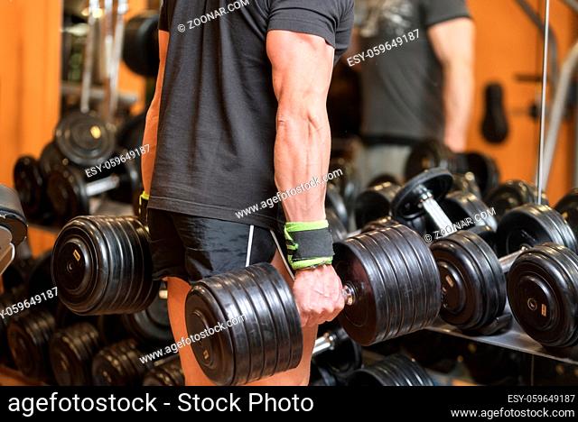 close up of muscular man holding heavy dumbbell in gym