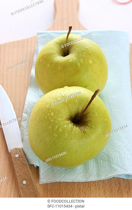 Two apples on a chopping board with a knife