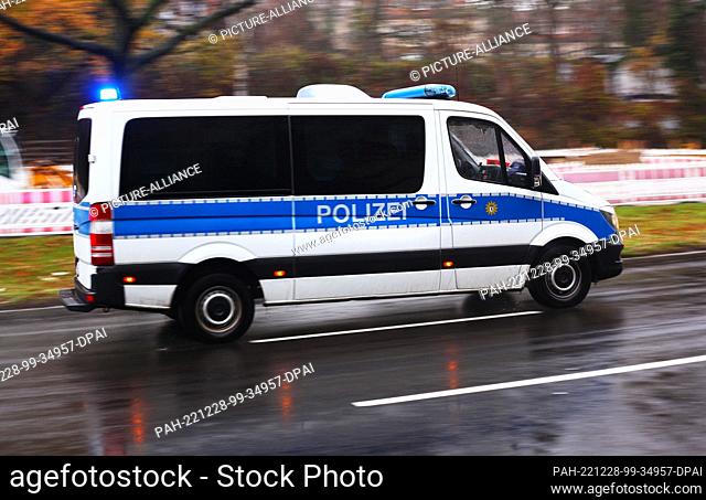 05 December 2022, Berlin: 05.12.2022, Berlin. A police squad car drives over a wet street with blue lights during a mission on a cloudy day in Steglitz