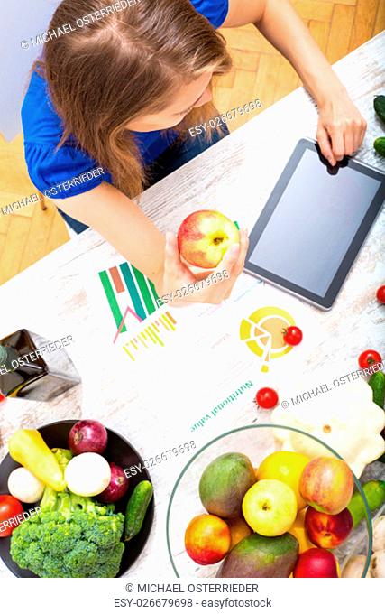 A young adult woman informing herself with a tablet PC about nutritional values of fruits and vegetables