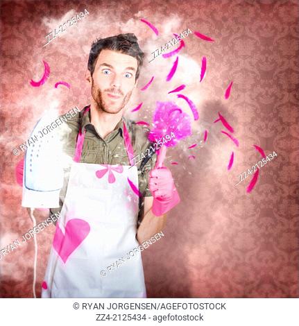 Funny creative portrait of a cleaning man dressed in feminine housework apron and gloves giving thumbs up with cheeky smile while holding hot iron and pink...