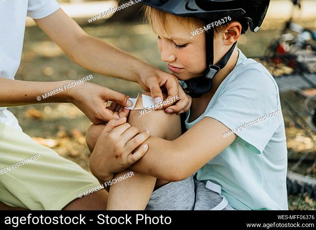 Boy putting bandage on younger brother knee sitting in public park