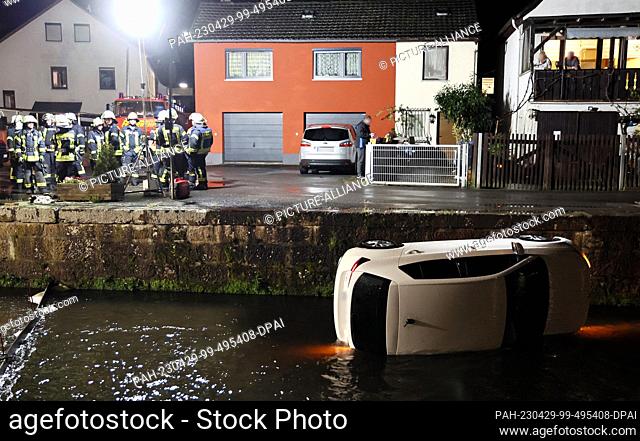 28 April 2023, Bavaria, Amorbach: Firefighters prepare to recover a car. A woman drove her car off the road in Amorbach (Miltenberg district) and fell into a...