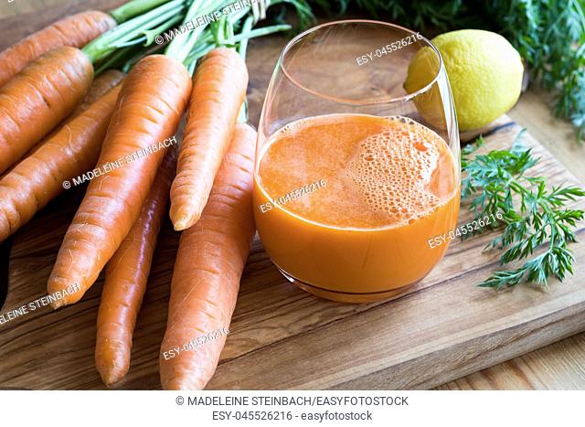 Carrot juice with fresh carrots and lemon on a wooden table