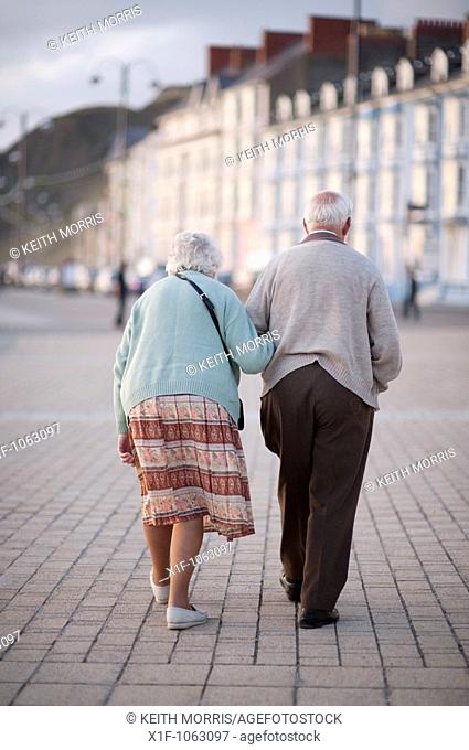 Elderly couple, old man and woman, walking in Aberystwyth promenade, summer evening, Wales UK
