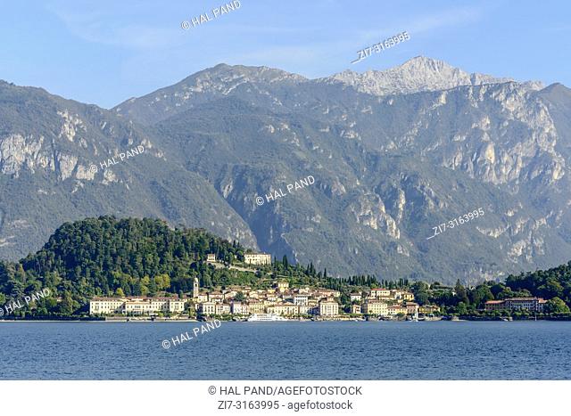 landscape of green lake coast of Como lake with Bellagio village, looming in background the Grigna peak range, shot in bright fall light from Cadenabbia, Como