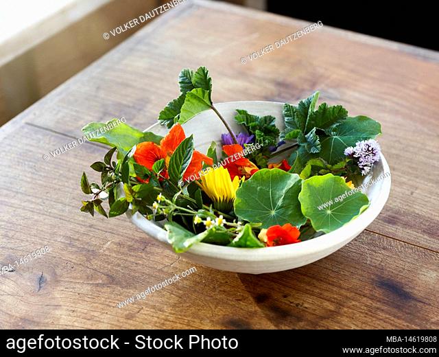 Bowl with edible flowers and herbs on a wooden table