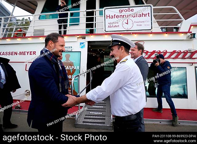 08 November 2023, Hamburg: The Norwegian Crown Prince Haakon (l) is welcomed by Captain Ali in front of the barge ""Commodore"" at the Elbphilharmonie pier for...
