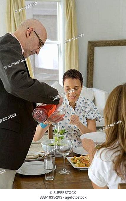 Side profile of a man pouring wine in a glass and two women sitting at a dining table