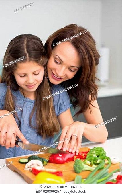 Woman with daughter chopping vegetables in kitchen