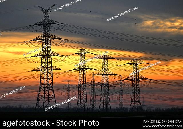 22 November 2023, North Rhine-Westphalia, Stommeln: The evening light shines orange-red behind electricity pylons. As a result of the Karlsruhe budget ruling