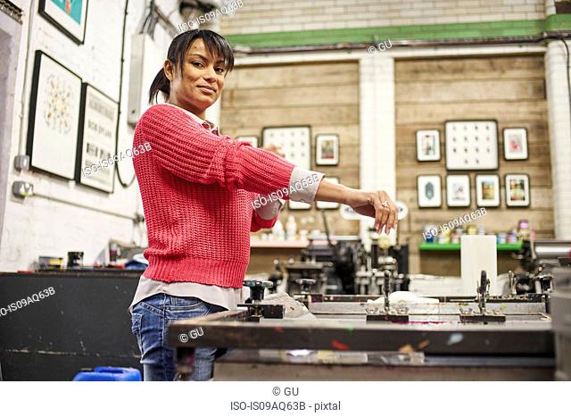 Mid adult woman rolling up sleeves to screen print in traditional print workshop