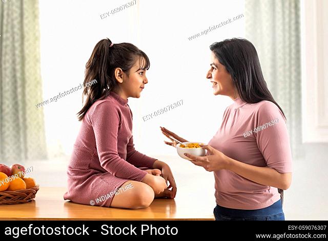 A MOTHER HAPPILY TALKING TO DAUGHTER WHILE GIVING HER BREAKFAST