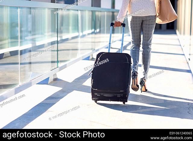 Low section of young biracial businesswoman walking with luggage in corridor at airport on sunny day