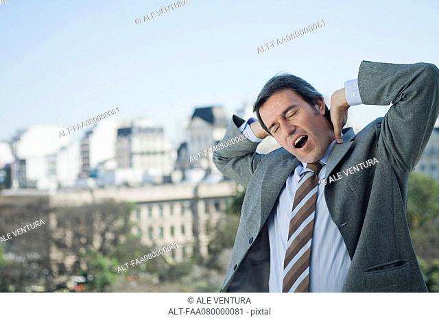 Mature businessman yawning and stretching outdoors