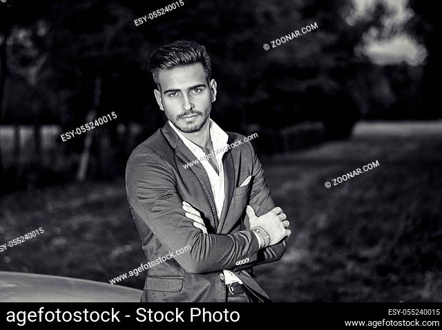 Portrait of young attractiave man in white shirt leaning on his new stylish polished car outdoor