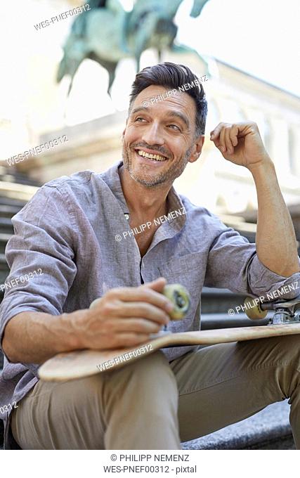 Portrait of laughing mature man with skateboard sitting on stairs