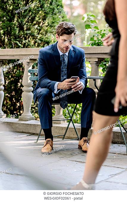Businessman in Manhattan sitting on garden chair using smart phone