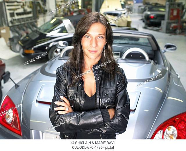 Portrait of a woman leaning on a gray convertible in a garage