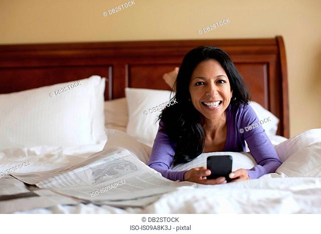 Mature woman lying on bed holding mobile phone, portrait