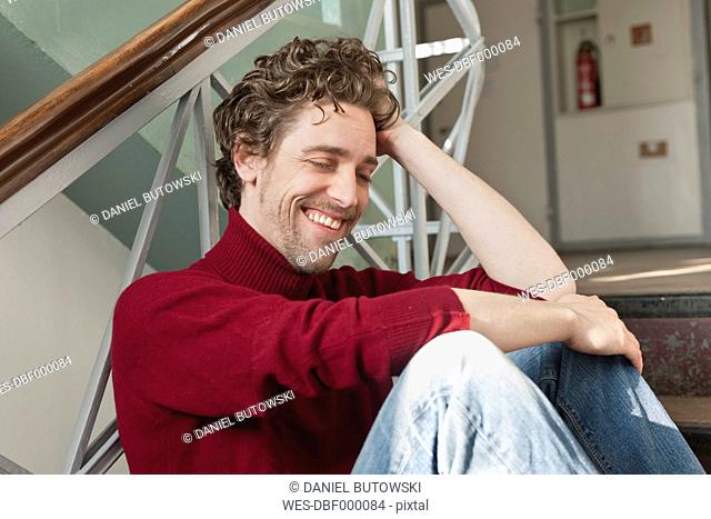 Mid adult man sitting on stairway, smiling