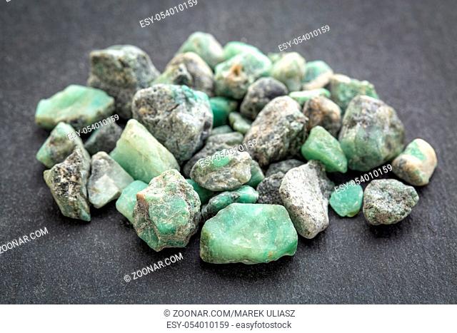 a pile of raw emerald gemstones (mineral beryl) with inclusions mined in Brazil on a gray slate stone