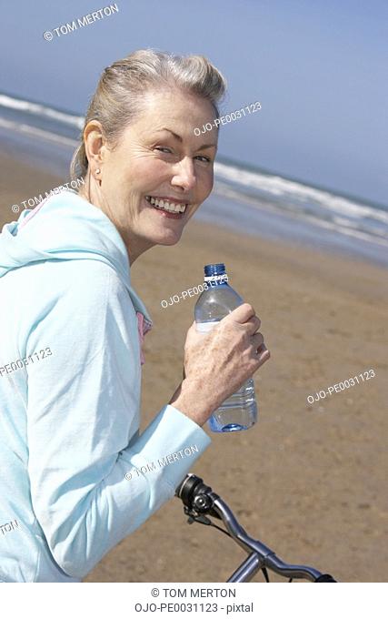 senior woman drinking water on a bike at the beach