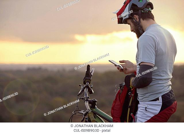 Male mountain biker looking at smartphone moorland