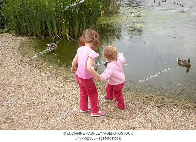Two lttle girls feeding the ducks by a lake