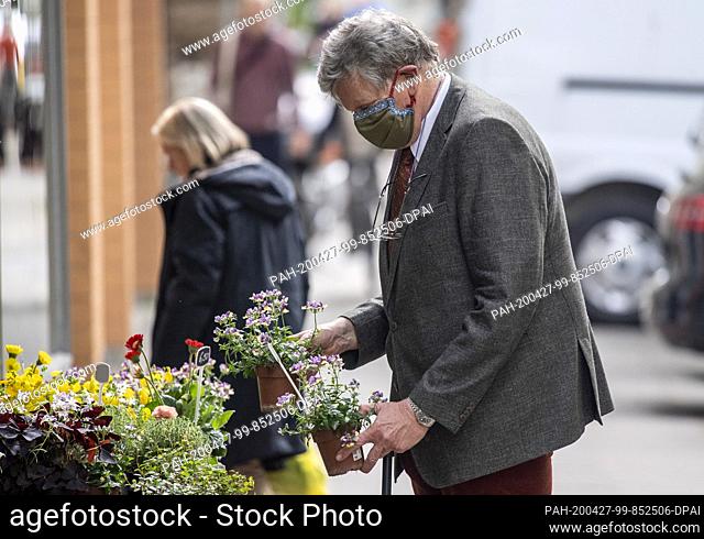 27 April 2020, Hamburg: A man is wearing a nose-mouth protective mask while holding flower pots in his hand in front of a flower shop