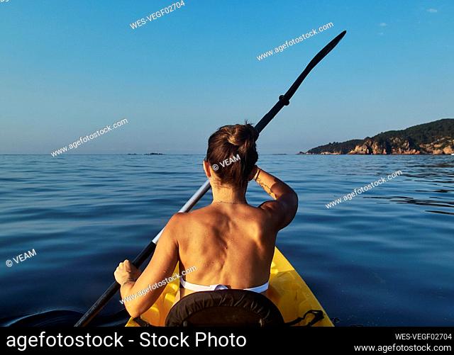 Woman kayaking while sitting in boat against clear blue sky