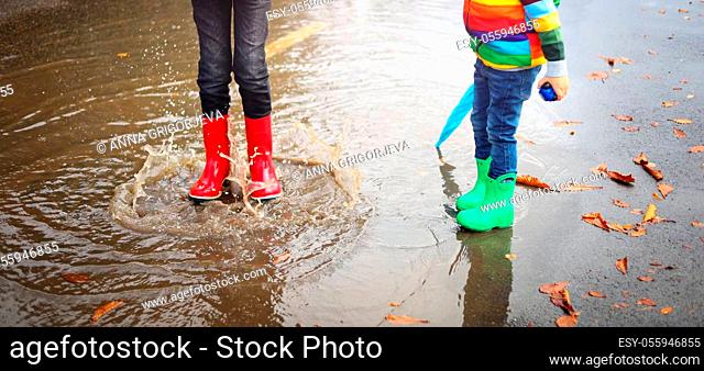 Child walking in wellies and jumping in puddle on rainy weather. Boy under rain in autumn outdoors