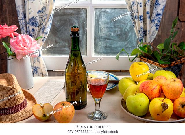 a Bottle and glass of cider with apples, near the window, in the rustic house
