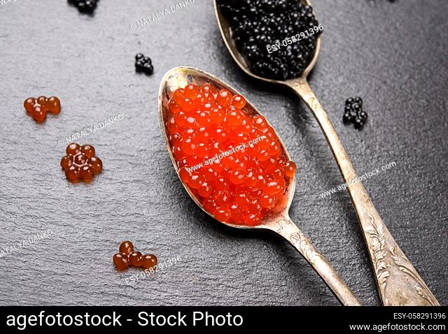 black caviar of paddlefish fish and red chum salmon caviar in a spoon, black background, top view