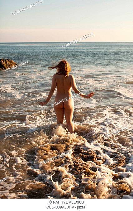 Rear view of naked mid adult woman running into the sea on El Matador Beach, Malibu, California, USA