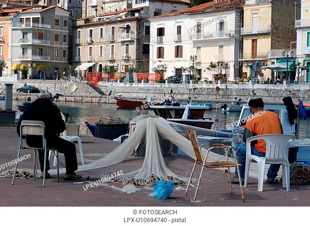 Scario harbour with boats, fisherman repairing nets, small fishing boats moored, and town of Scario beyond, on sunny, summer morning