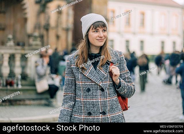 Smiling young woman wearing knit hat standing at footpath