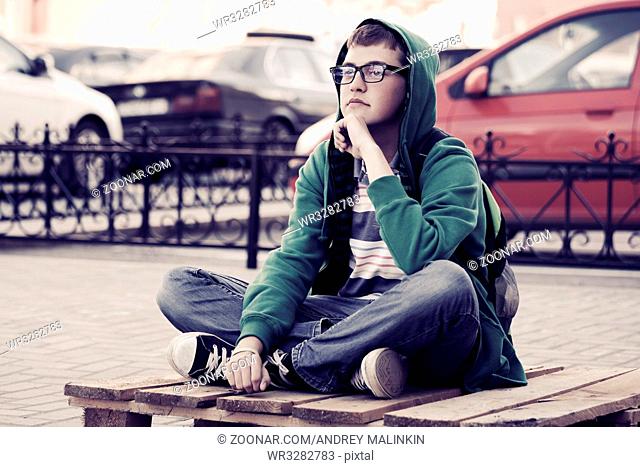 Fashion teen boy sitting on a city sidewalk