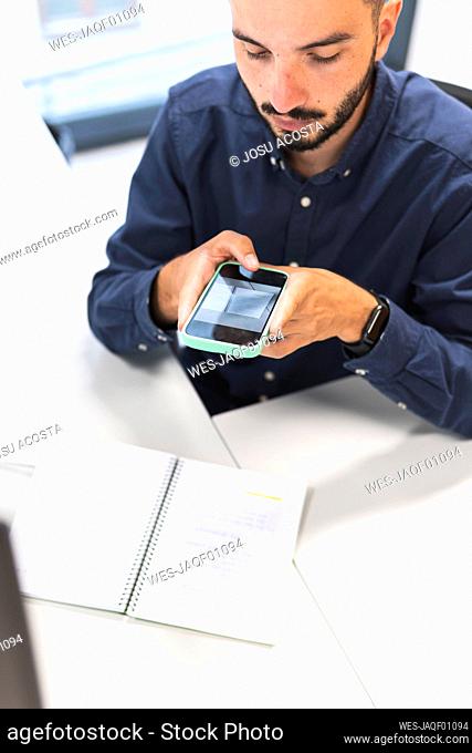 Young businessman photographing through smart phone at desk
