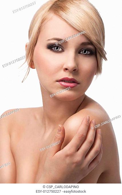 close up beauty portrait of a young and cute blond girl with hair style over white, she looks in to the lens and touches her left shoulder with a right hand