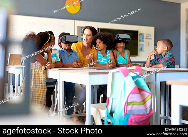 Caucasian young female teacher looking african american elementary students wearing vr glasses