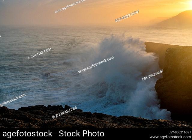 A view of huge storm surge ocean waves crashing onto shore and cliffs at sunrise