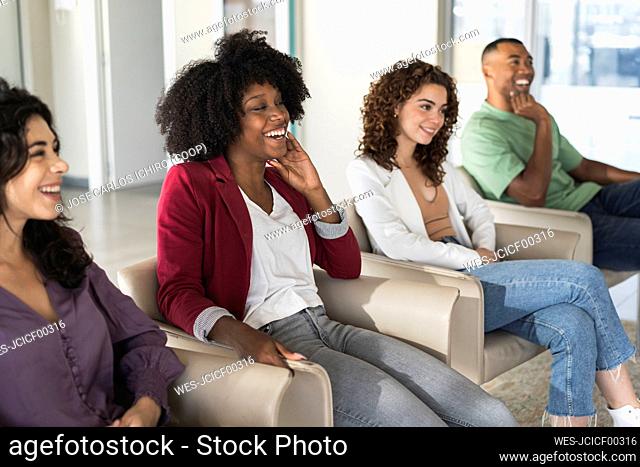 Happy businesswoman with Afro hairstyle sitting amidst colleagues in office