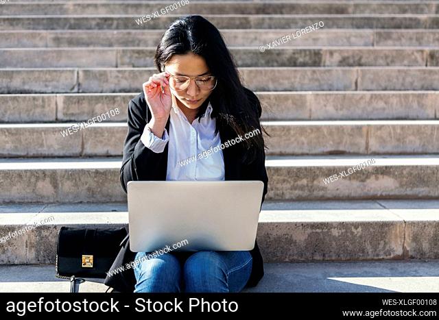 Young businesswoman sitting on stairs outdoors using laptop