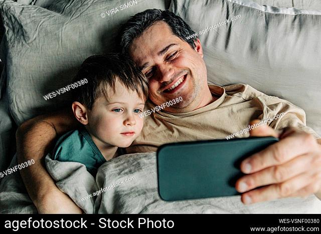 Father and son taking selfie using smart phone on bed