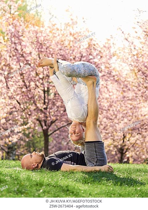 Couple training acro yoga in a park, cherry blossoms on background, May in south of Finland
