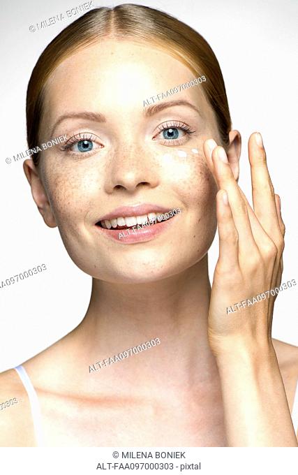 Young woman applying undereye cream