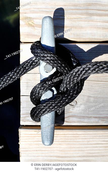 A black rope used to tie up a boat, around a bollard