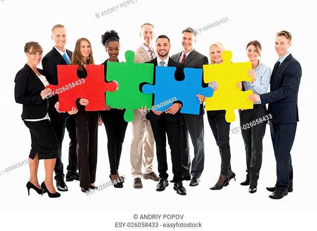 Full length portrait of happy business team holding jigsaw pieces against white background