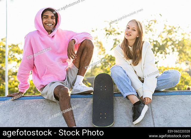Multicultural group of young friends bonding outdoors and having fun - Stylish cool teens gathering at urban skate park